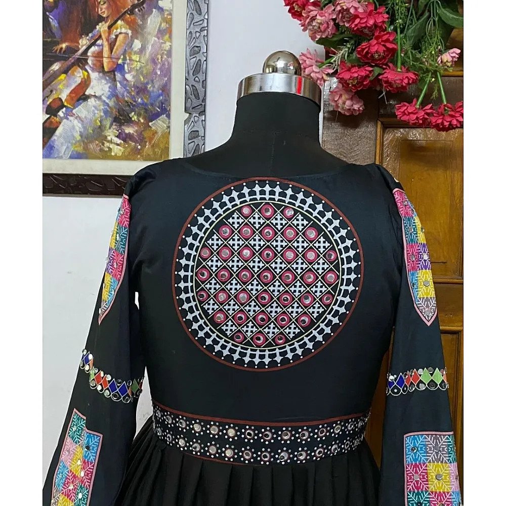 A close-up view of a black traditional Gujarati lehenga choli displayed on a mannequin, featuring intricate mirror work and colorful embroidered patterns on the back and sleeves.

