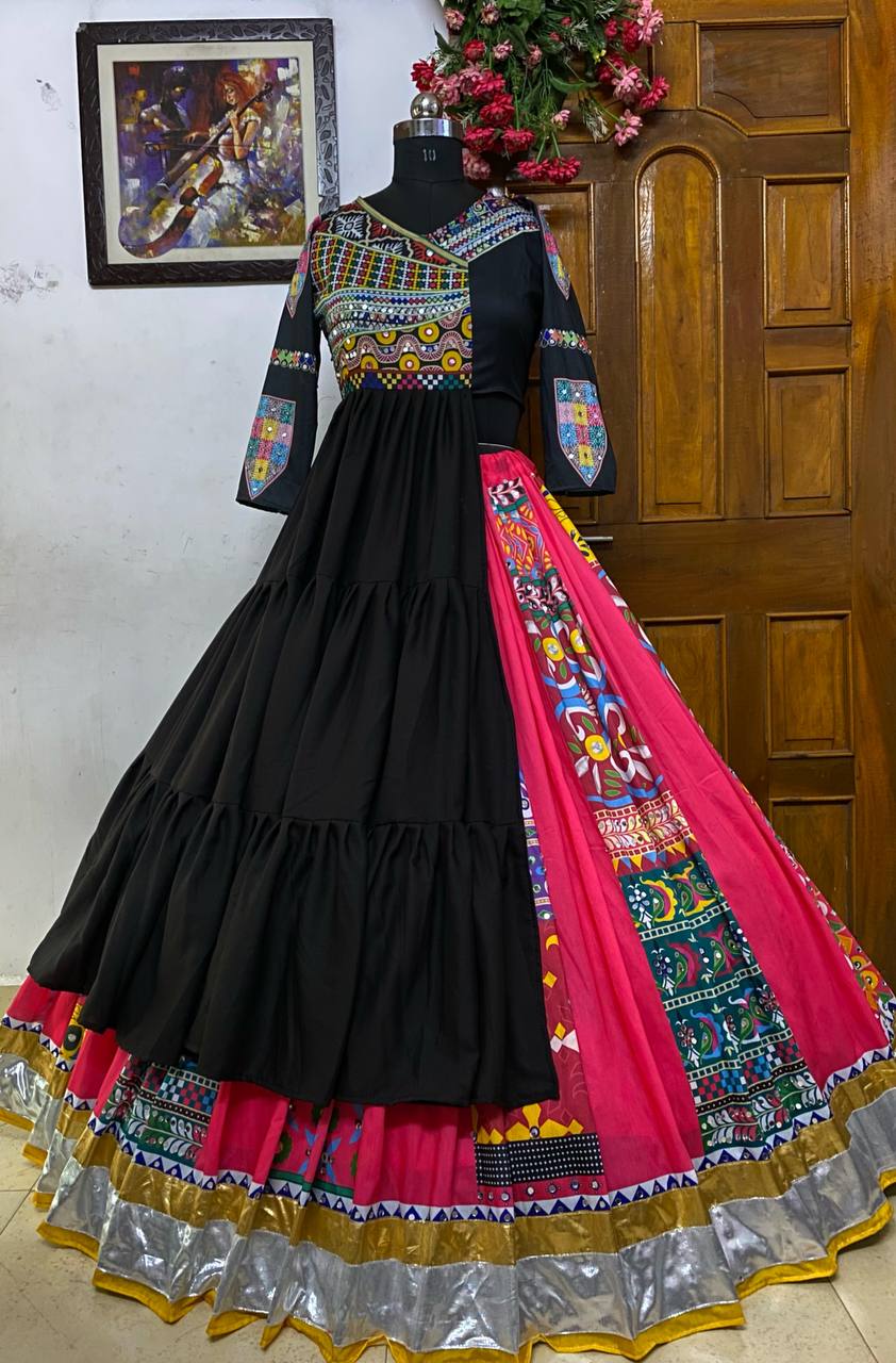 A beautifully designed black and pink traditional Gujarati lehenga choli displayed on a mannequin, featuring intricate mirror work, colorful embroidery, and a flared silhouette with silver and gold border detailing.

