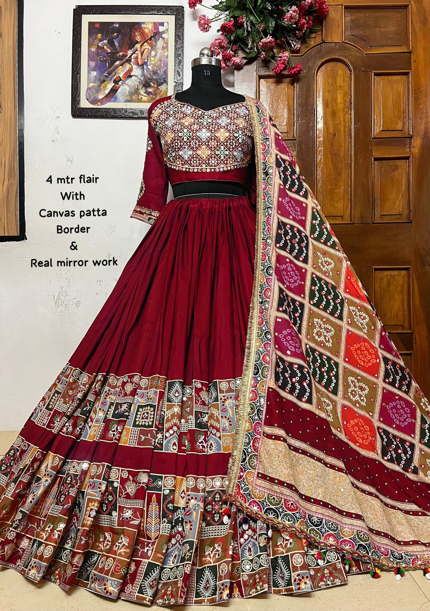 A beautifully designed maroon Navratri lehenga choli displayed on a mannequin. The outfit features intricate mirror work, a 4-meter flair, a canvas patta border, and a multicolored dupatta with traditional Gujarati prints. Perfect for Garba nights and festive celebrations.