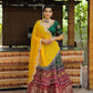 A woman gracefully poses in a traditional green and maroon lehenga choli, featuring intricate embroidery and a vibrant yellow dupatta, perfect for festive occasions.