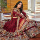 A woman wearing a stunning maroon Navratri lehenga choli featuring intricate traditional prints, mirror work, and a matching dupatta, perfect for Garba nights.







