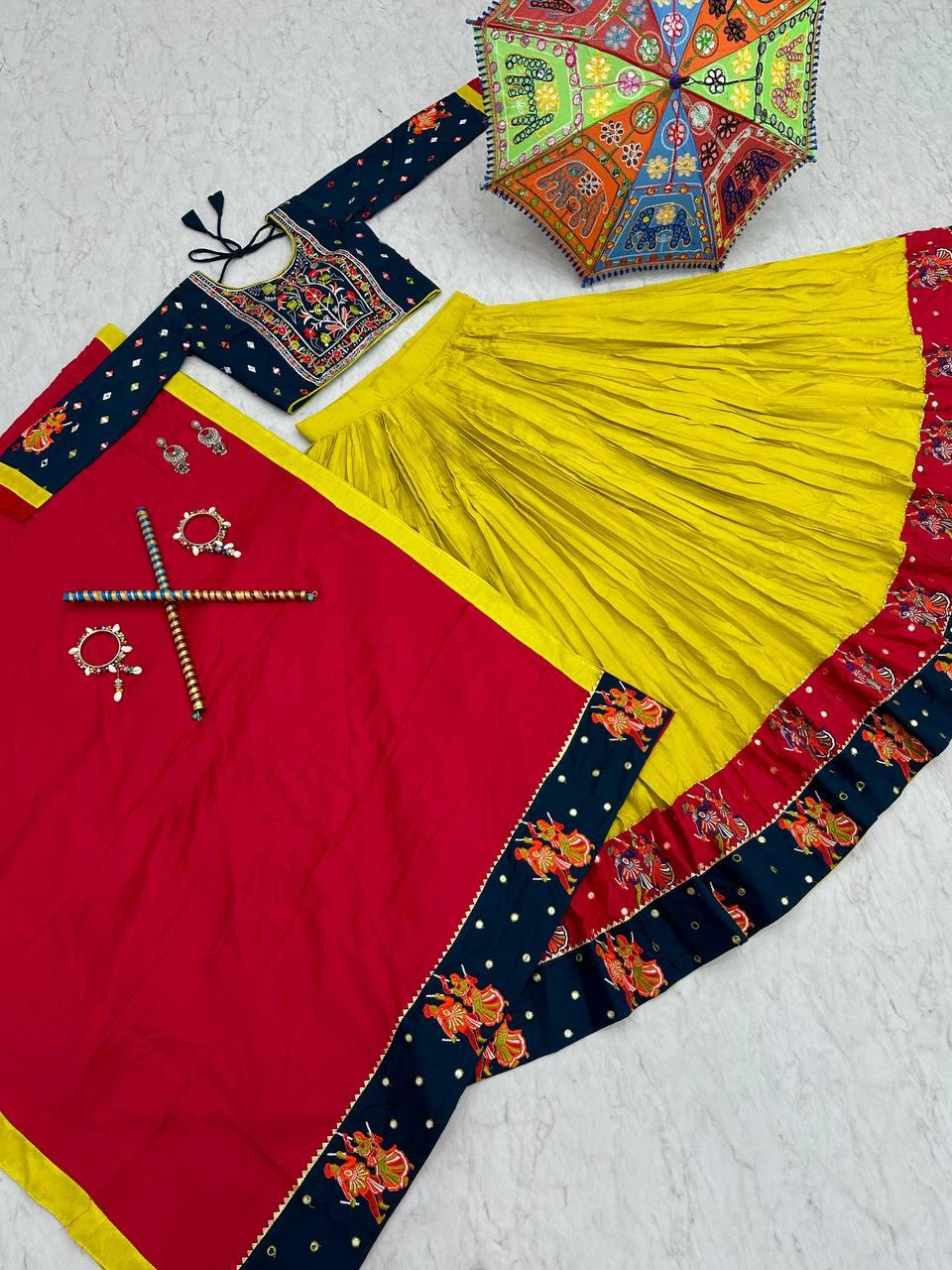 A beautifully displayed traditional Gujarati lehenga set, including a vibrant yellow skirt with a blue and red embroidered border, a navy blue embroidered blouse, and a red dupatta with matching detailing. The ensemble is complemented by a colorful Rajasthani umbrella, traditional jewelry, and dandiya sticks, emphasizing the festive spirit of Navratri and Garba celebrations.







