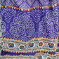 A vibrant purple fabric featuring intricate white Bandhani (tie-dye) patterns in symmetrical designs. The fabric is adorned with colorful decorative borders, including multicolored tassel-like embroidery and a detailed elephant motif strip with floral elements. The traditional design and rich colors make it ideal for ethnic wear.