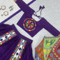 Flat-lay of a purple Navratri lehenga set with intricate Gamthi embroidery, including a matching blouse, skirt, white dupatta, silver jewelry, and a colorful embroidered umbrella.
