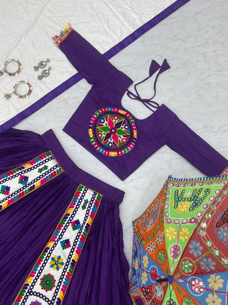 Flat-lay of a purple Navratri lehenga set with intricate Gamthi embroidery, including a matching blouse, skirt, white dupatta, silver jewelry, and a colorful embroidered umbrella.