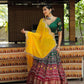 A woman elegantly showcases a green and maroon lehenga choli with intricate embroidery, paired with a vibrant yellow dupatta, perfect for festive celebrations.