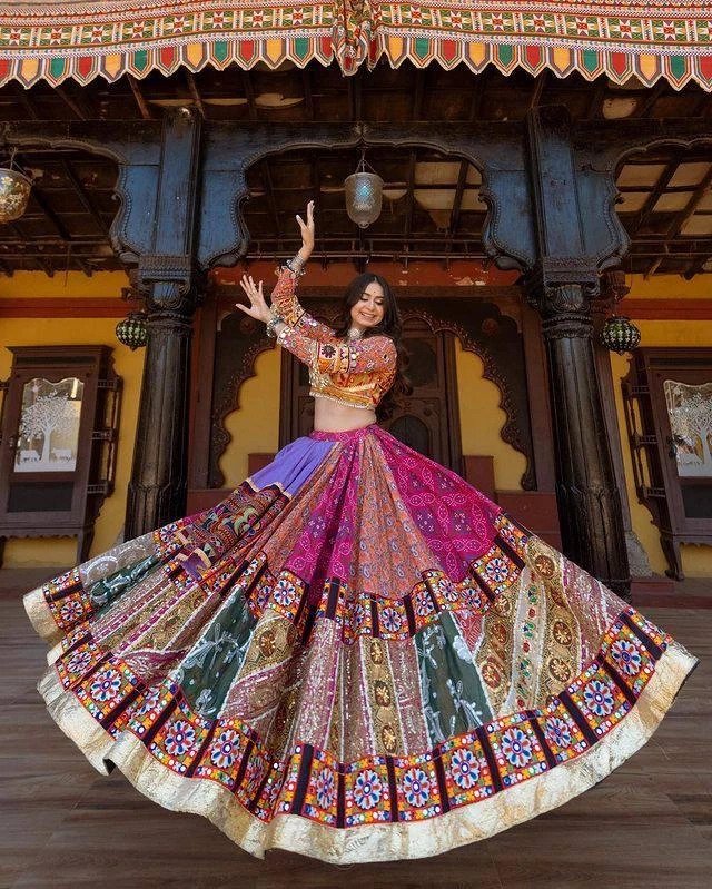A woman gracefully twirling in a colorful Navratri Lehenga Choli, featuring intricate mirror work, rich embroidery, and a voluminous flair, perfect for Garba and festive celebrations.