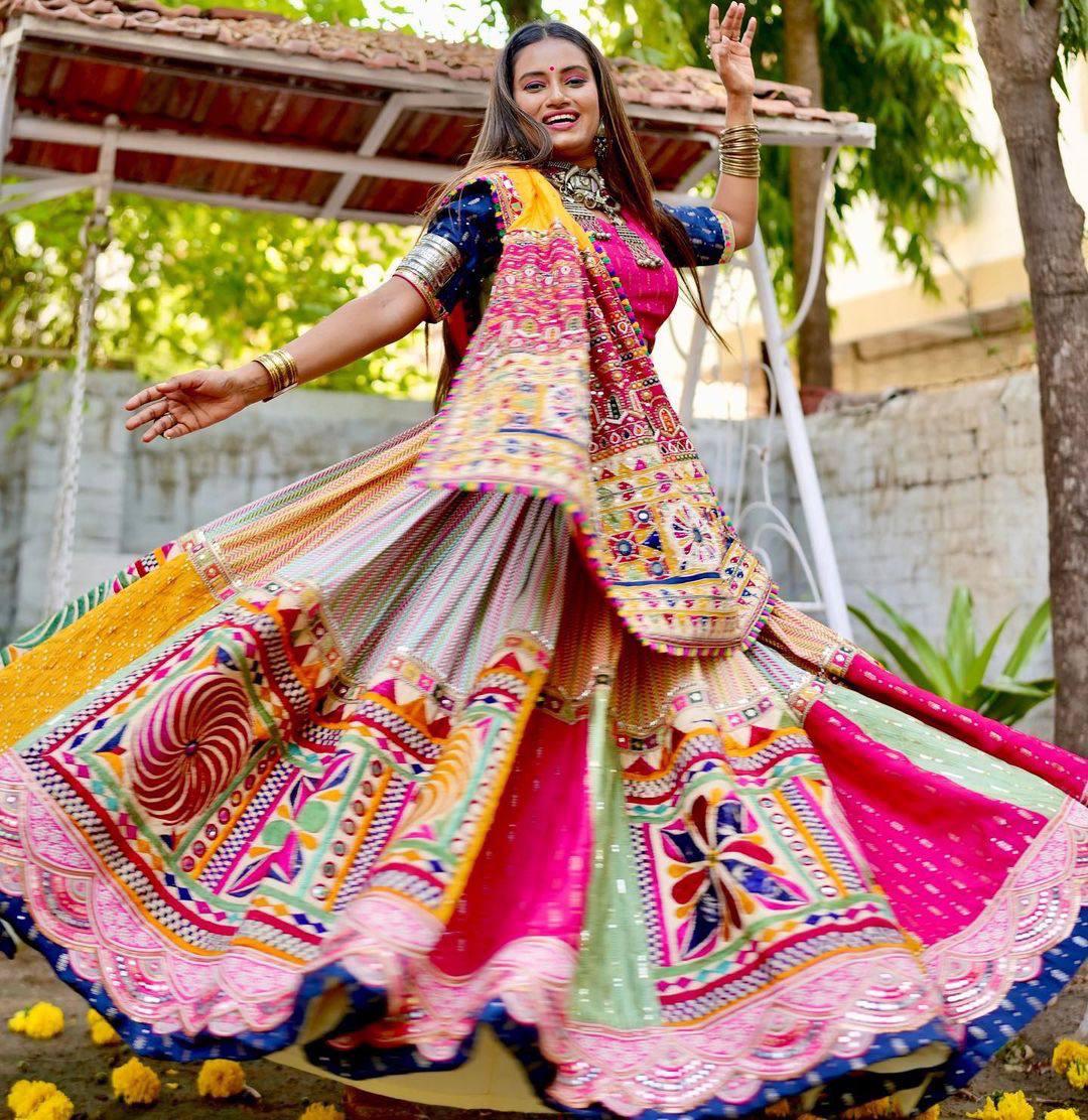 A woman twirls in a colorful Navratri lehenga adorned with intricate digital prints, real mirror work, and rich embroidery, showcasing festive elegance.







