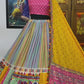 A beautifully designed Gujarati lehenga displayed on a mannequin, featuring a multicolored skirt with detailed patchwork, a pink and blue embroidered blouse, and a bright yellow dupatta with traditional mirror work and embellishments. A painting of Radha-Krishna is visible in the background.








