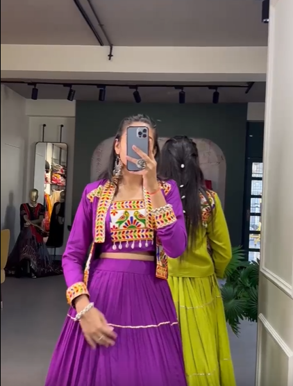 A collection of traditional lehengas in multiple colors, featuring intricate embroidery and gold detailing, displayed in a boutique setting with elegant decor and designer outfits in the background.