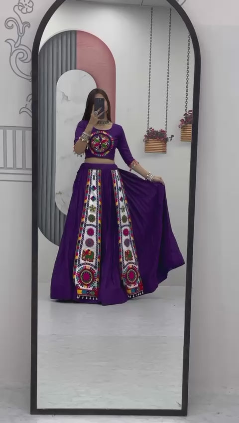 A woman gracefully showcases her traditional Navratri lehenga in front of a mirror, twirling to highlight the intricate Gamthi embroidery and vibrant colors. She admires the detailed patterns on her outfit, adjusting her dupatta and jewelry, radiating confidence and elegance in the festive attire.