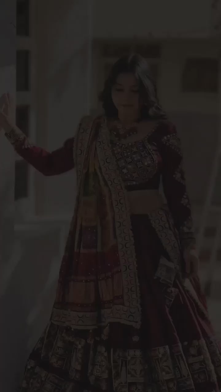 A woman dressed in a stunning maroon designer lehenga gracefully swirls, showcasing the outfit's elegant 4-meter flair. The lehenga features intricate mirror work, a canvas patta border, and vibrant traditional prints. As she twirls, the rich fabric and detailed craftsmanship are highlighted, making it a perfect attire for festive occasions like Navratri and weddings.