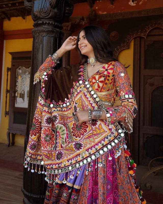 A woman wearing a vibrant Designer Navratri Lehenga Choli adorned with intricate mirror work, embroidery, and tassels, perfect for Garba and Dandiya nights.